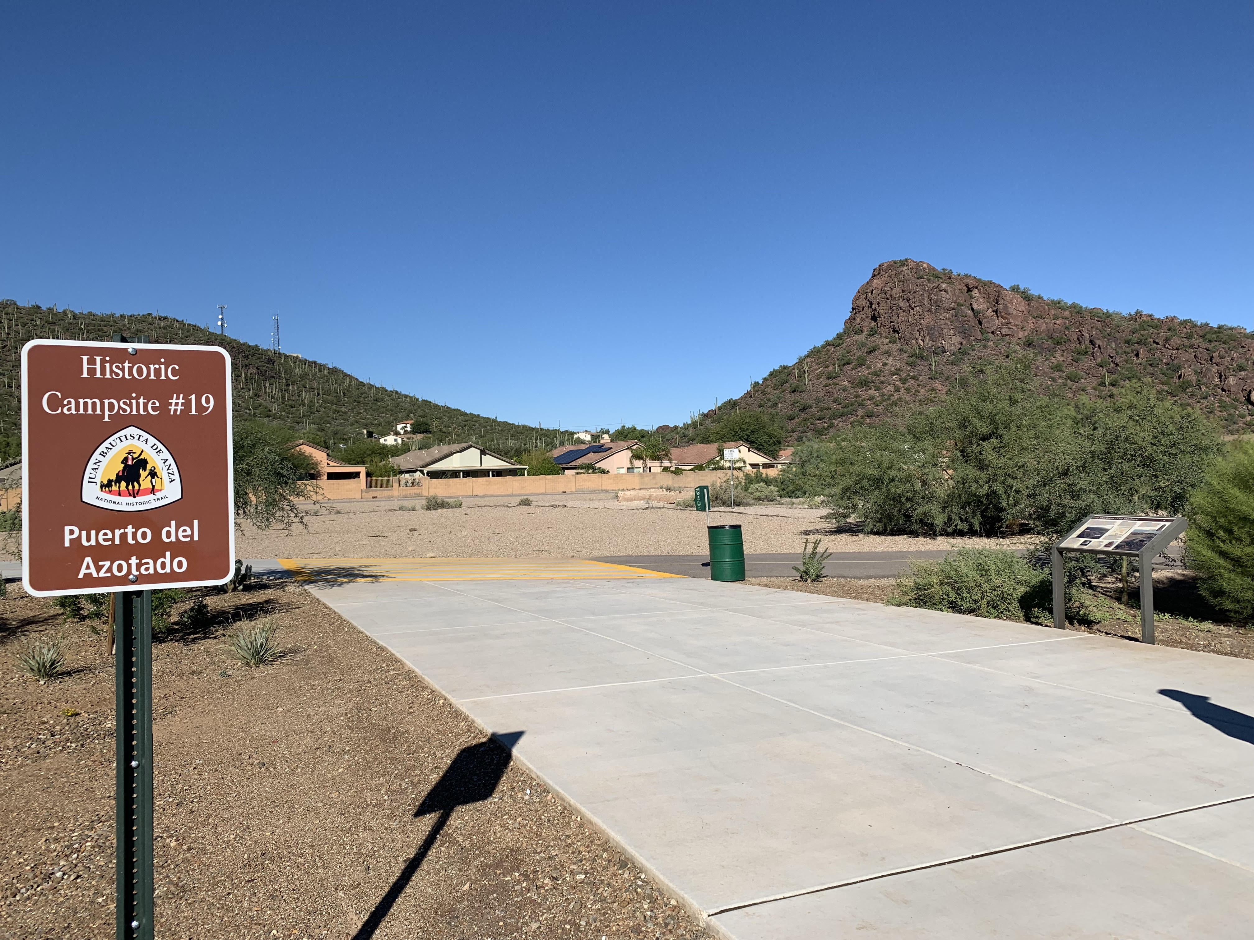 A trailhead sits at the base of the pass where the expedition travelled through. You can see the saddle of the mountains. A sign marks it as part of the Anza Trail reading 