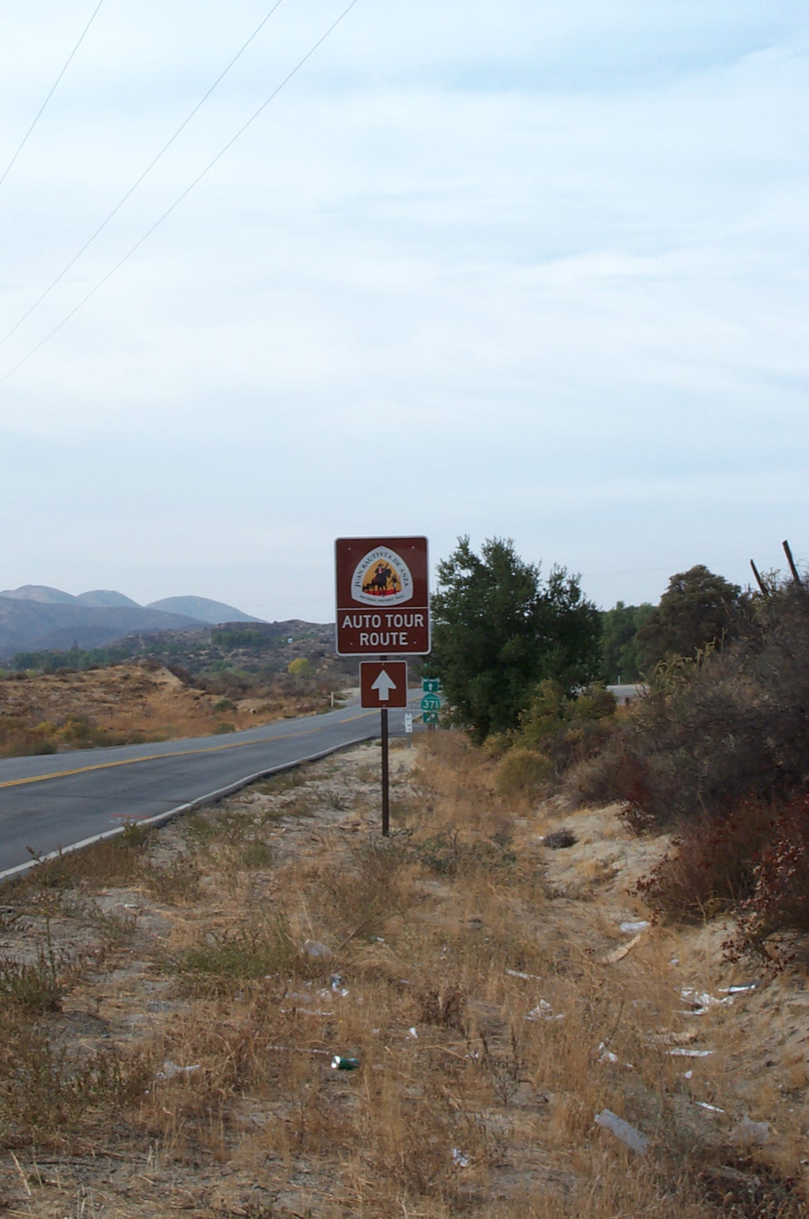 An Anza Trail Auto Route sign along a highway with mountains in the background.