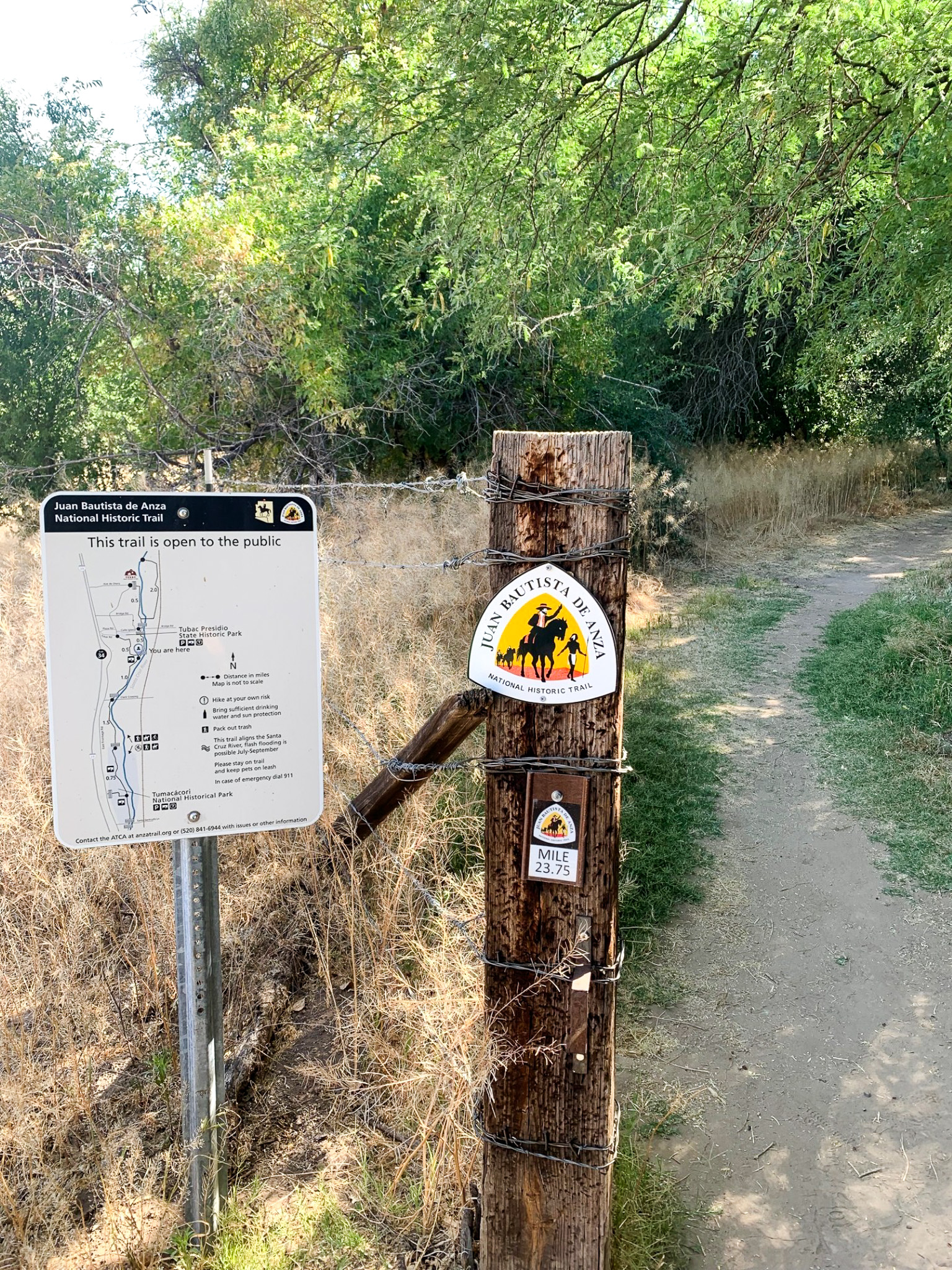 A post with a map of the Anza Trail stands next to a wooden post with an Anza Trail logo and mile marker