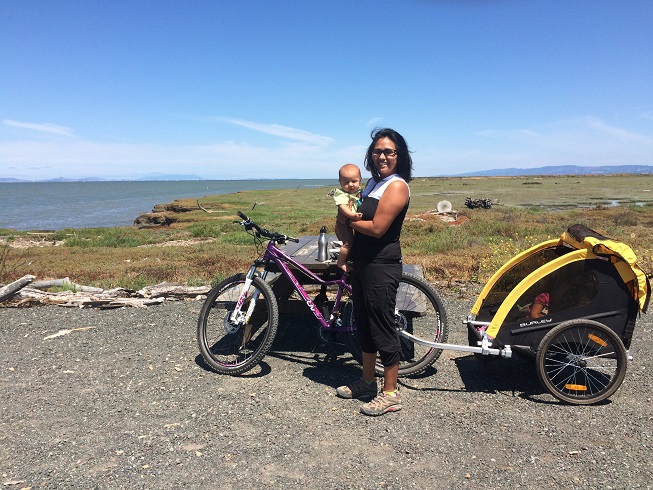 Woman standing and holding her baby in front of her bike and bike trailer