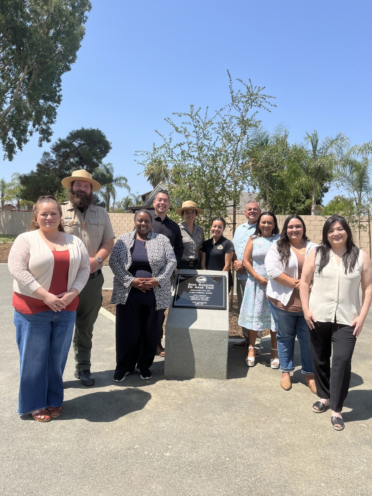 A group of people stand outside smiling next to a plaque that says 