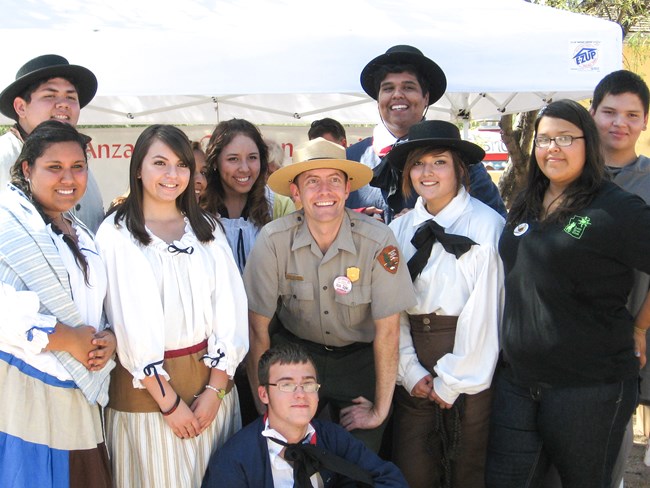 A group of young adults in colonial dress pose next to a park ranger for a photo