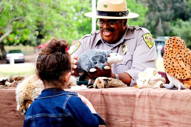A little girl stands at a table where a park ranger holds a stuffed animal