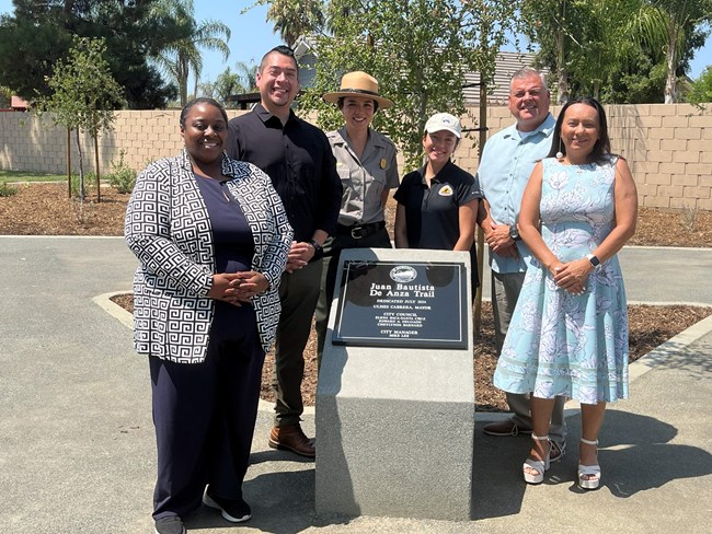 Five people pose for a picture in front of a memorial plaque
