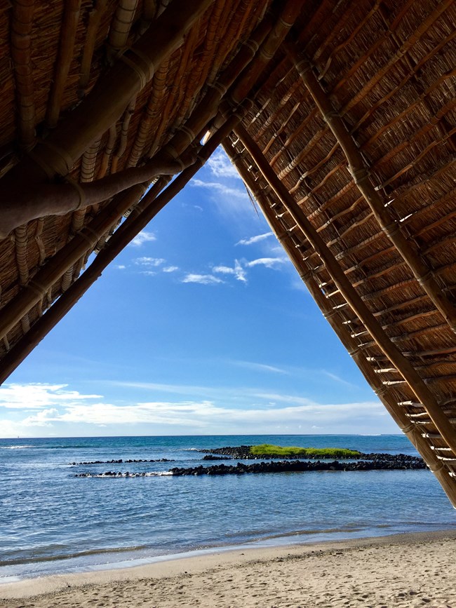 View of Honokohau beach from underneath the roof of a traditional hale