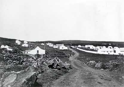 Early black and white photo of the Kalawao settlement with a dirt road heading towards many buildings