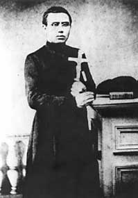 A black and white image of a man, Father Damien, holding a cross.
