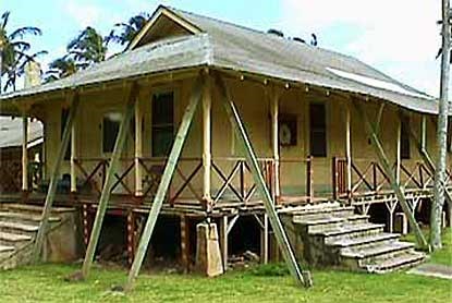 A light-colored building with a porch and large stabilizer beams running from the ground to the roof.