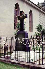 Father Damien's grave with a tall cross statue outside of a church building.