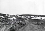 A black and white image of a dirt road leading to buildings