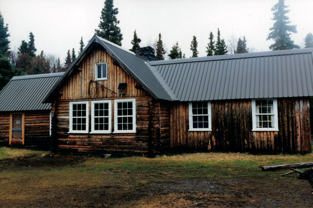 large log building with 2 windows on right wing, 3 windows on main structure and door on left wing.