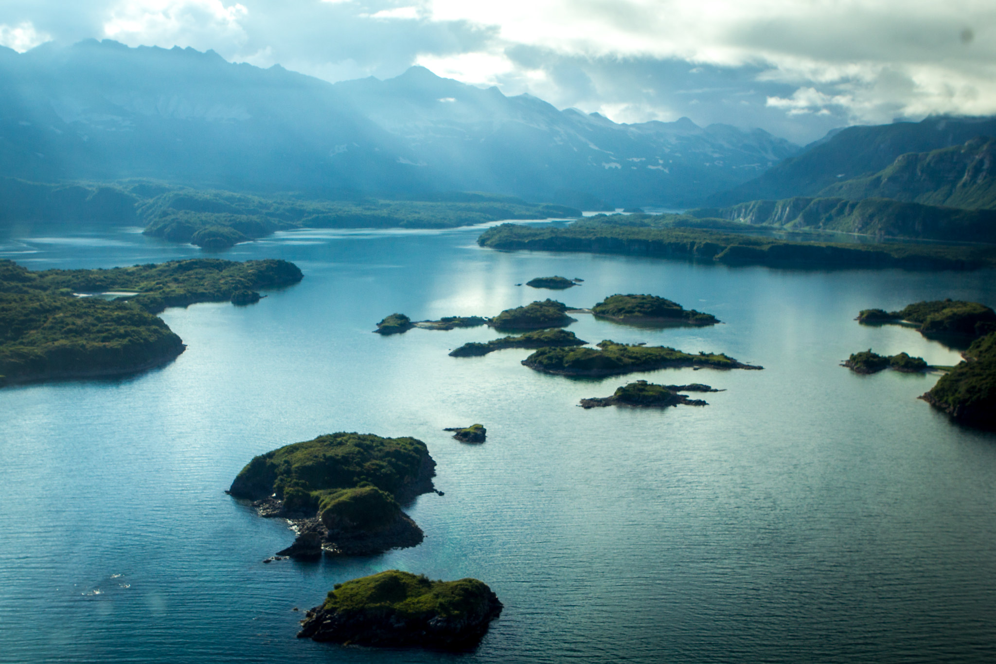 View of the bay from a plane, small islands dot blue water with a mountain mainland in the background.