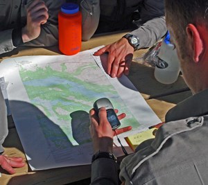 Rangers entering waypoints on a GPS as they study a topographic map