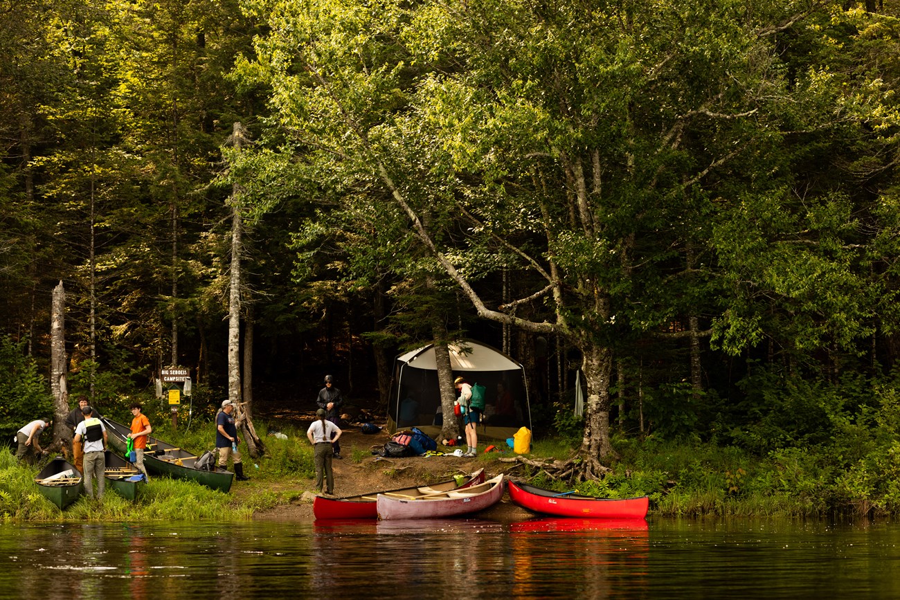 A group of campers near the bank of a large river, getting ready to canoe back after a camping trip.