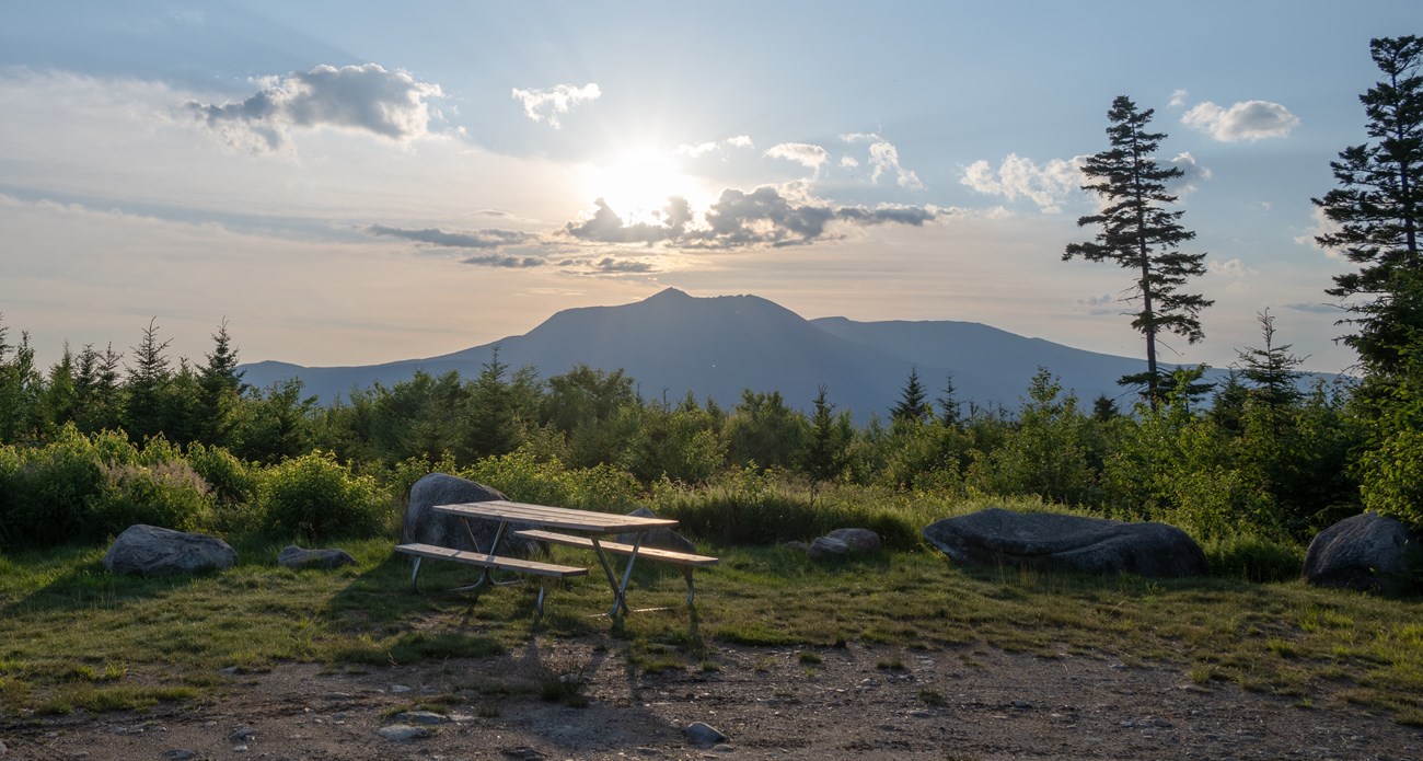 A picnic table sits in a beam of light at the loop road Overlook with Katahdin in the background.