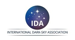 International Dark-Sky Association Logo, a dark purple and blue gradient filled circle with the letters I D A on the bottom and starbursts and small spheres mimicking stars inside the large circle.