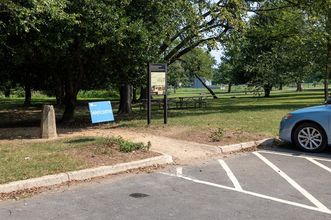 A small concrete ramp from a paved parking lot up to a gravel path leading towards a park.