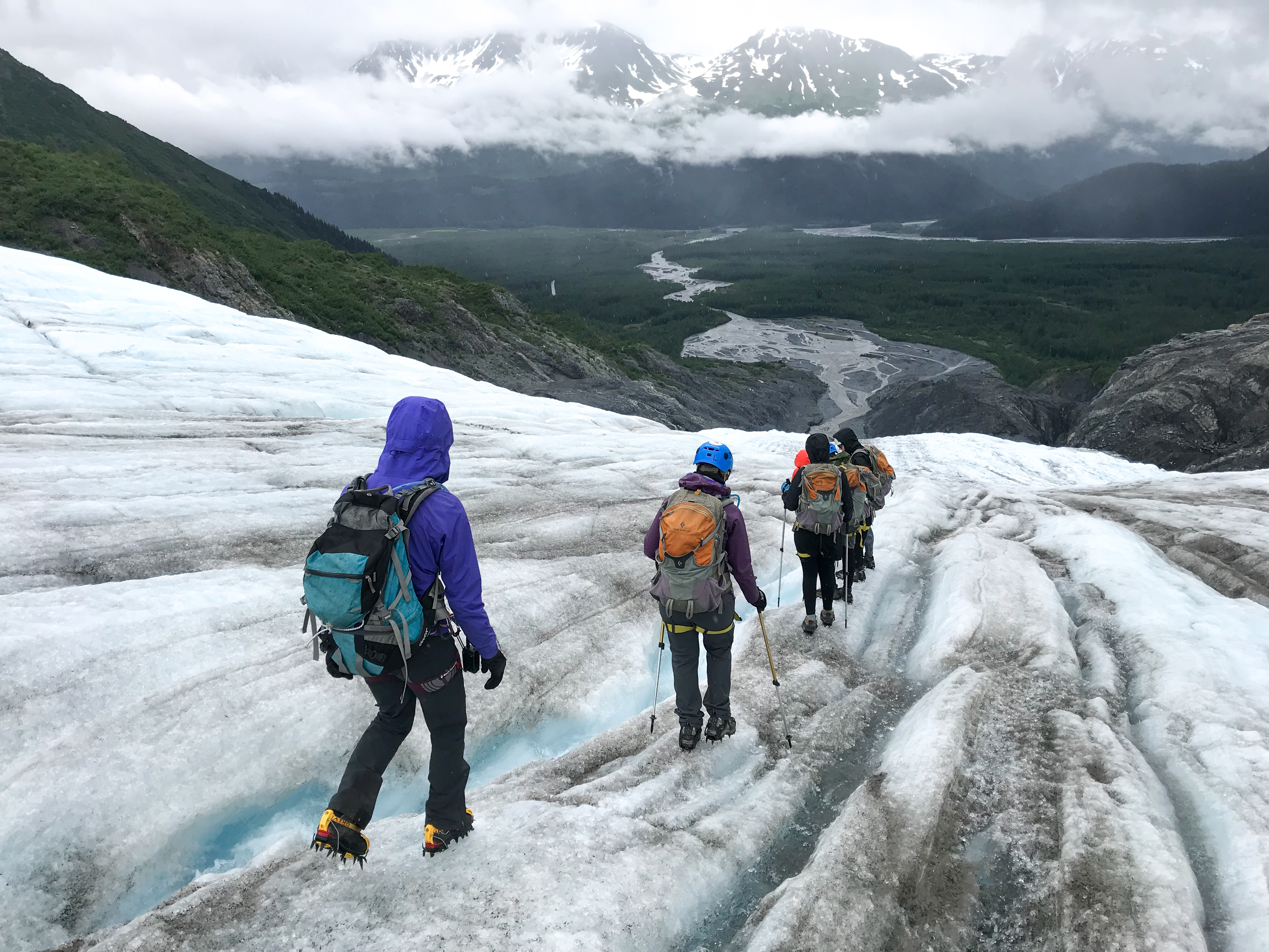 A group of hikers in safety gear walk on a blue glacier
