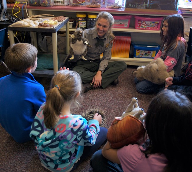 A park ranger in a classroom talking to a group of children. The Ranger has a puppet on their hand.