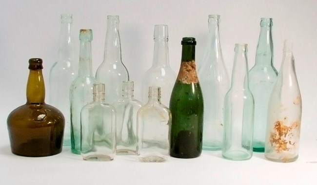 A number of old glass bottles sit in front of a plain white background.