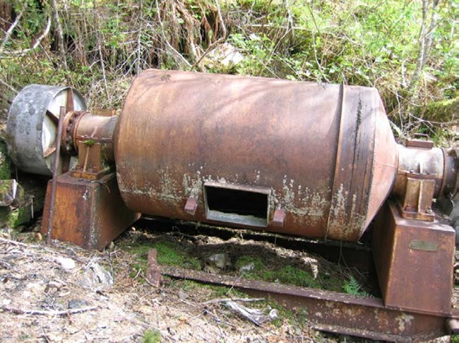 A large, rusty cylinder on mounts with a pully on one end.