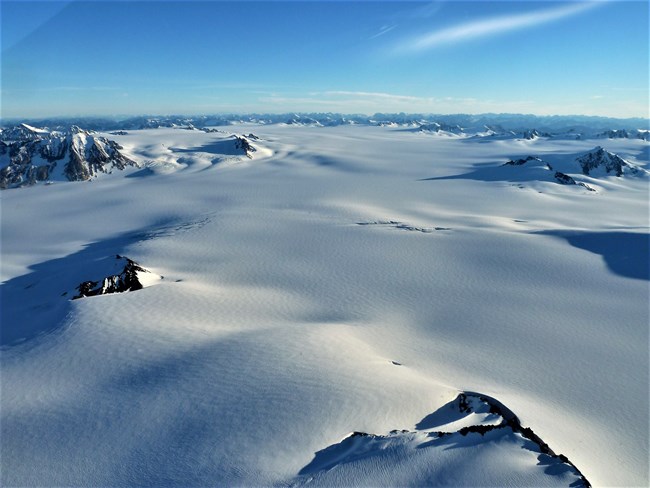 a large area of ice that is covered by snow.  Mountain peaks appear through the snow and ice.