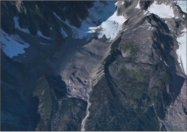 an aerial view of a glacier and some mountain ridges.  A pile of dirt and debris that has been lift by the glacier sits at its toe