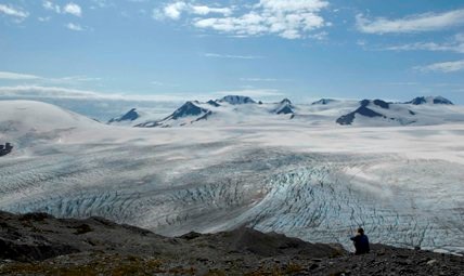 A hiker sits at the end of the Harding Icefield Trail, and looks out over the ice field itself.