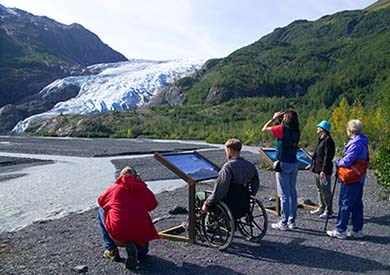 A diverse group of people (including a wheelchair) looking across the outwash plain at a valley glacier in the distance.