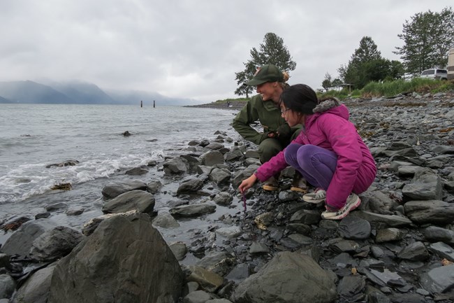 A park ranger and kid look out at water