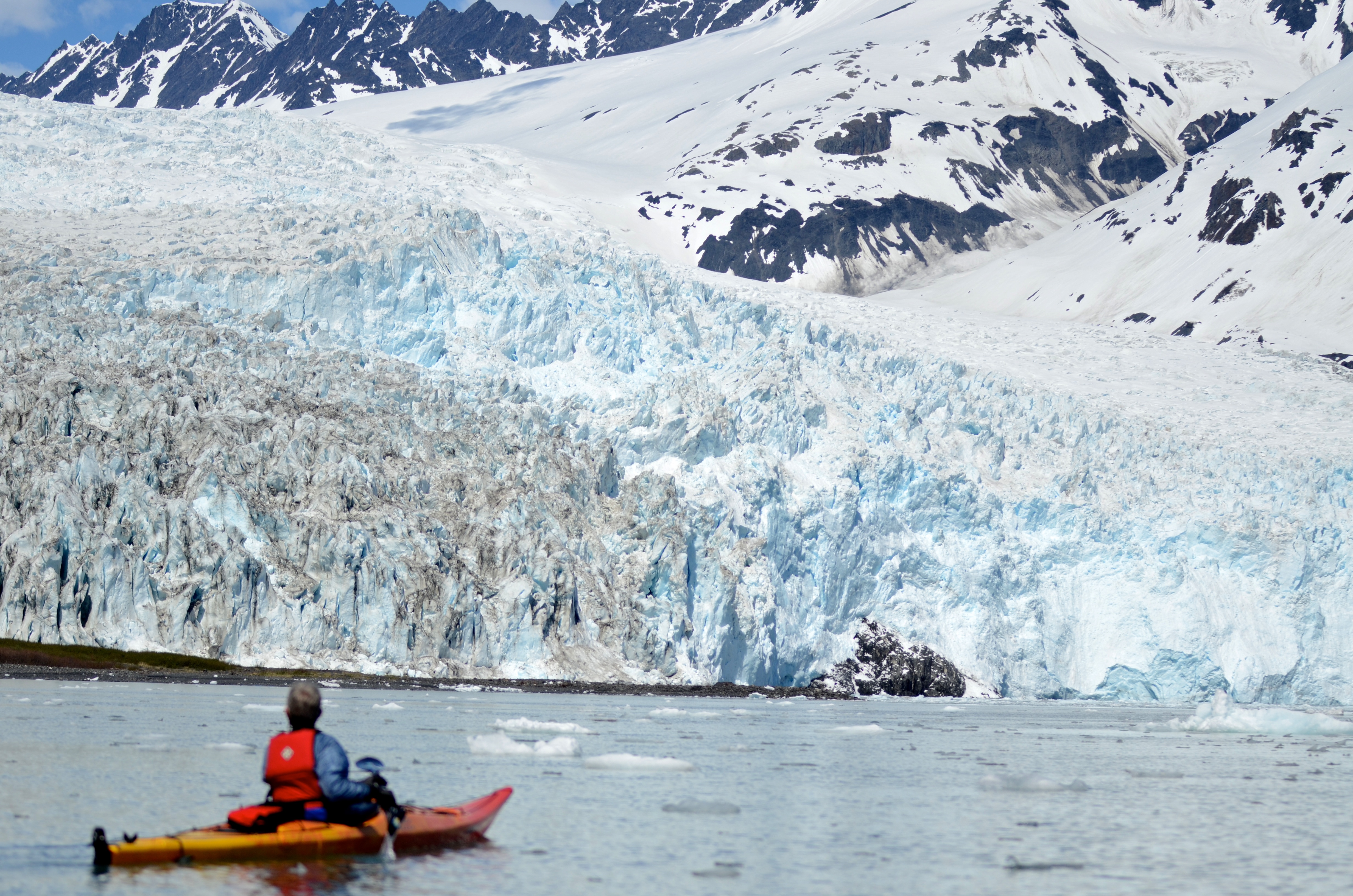 A person paddles with a large tidewater glacier in the distance