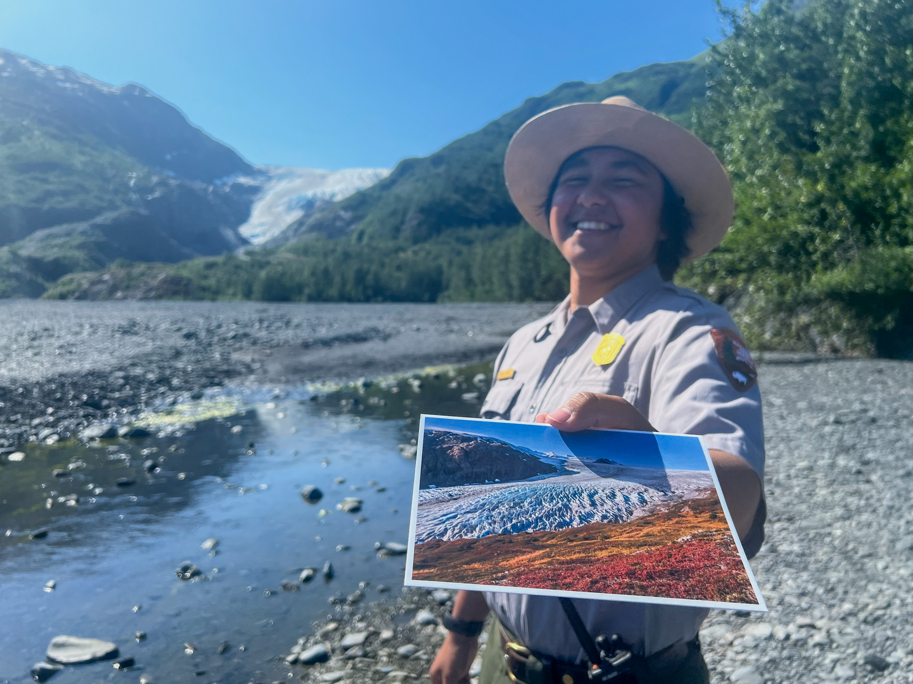 A park ranger holds a postcard out with a glacier on it