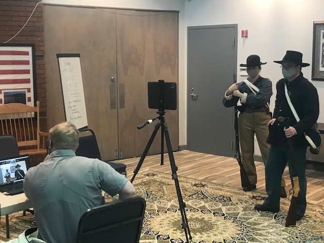 Two rangers dressed as Civil War soldiers stand in front of tripod and camera.