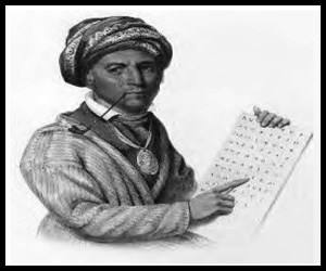 Man with dark skin wears a collared shirt under a long-sleeved cardigan type sweater. A turbin is wrapped around his head, a round medallion hangs from his neck, and a long pipe dangles from his lips. He points to a board with letters on it.
