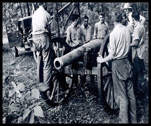Black and White: 7 men stand around an old cannon barrel outside.