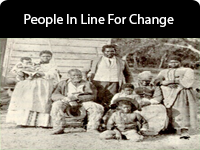 4 adults, 3 kids, and a baby, all black, pose in front of a house.