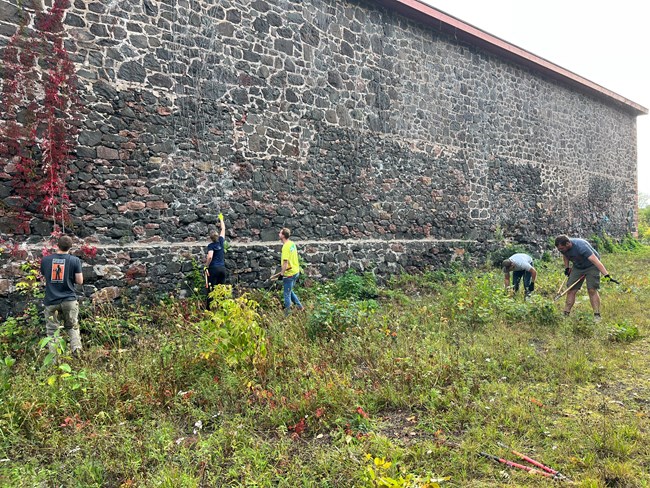 Volunteers use hand tools to clear vegetation from the Pattern Storage building in Calumet’s Industrial Corridor.