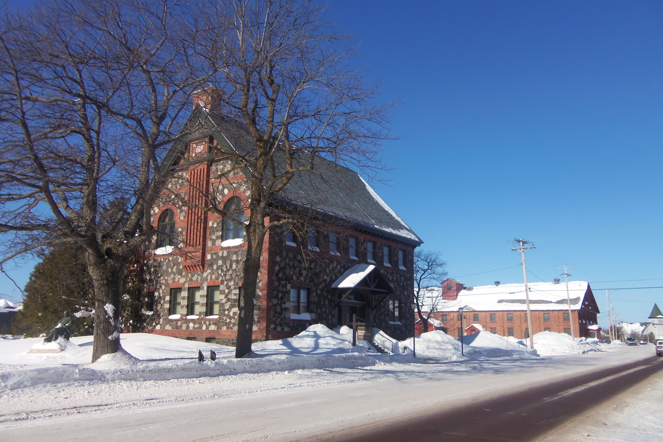 A brick and stone building surrounded by piles of snow and barren trees.