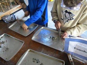 Hands use hammers to crush rock on a table.