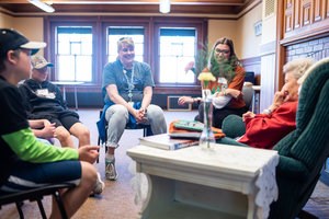 Adults and children sit in chairs in a circle talking with each other.