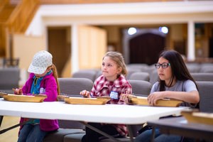 Three seated students listen to directions for the harp laying on a table in front of them.