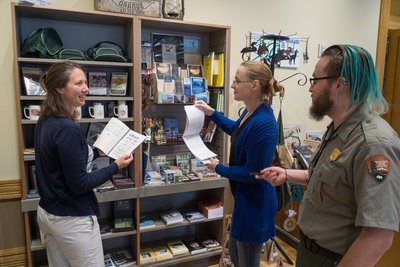 Two people look at books and ask questions of a park ranger.