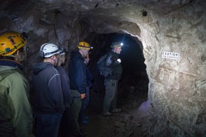 A group of people with hardhats and head lamps explore a former underground copper mine with a tour guide.