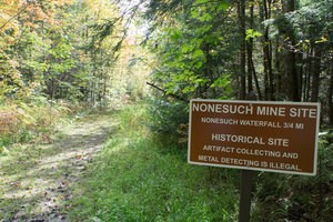 A brown sign with white lettering next to a trail reading "Nonesuch Mine Site."