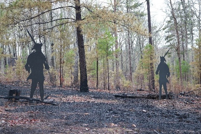 Two metal sillhouettes of soldiers are in a field that has burned ground.