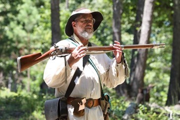 A living historian wearing a 18th century hunting shirt is holding a musket.