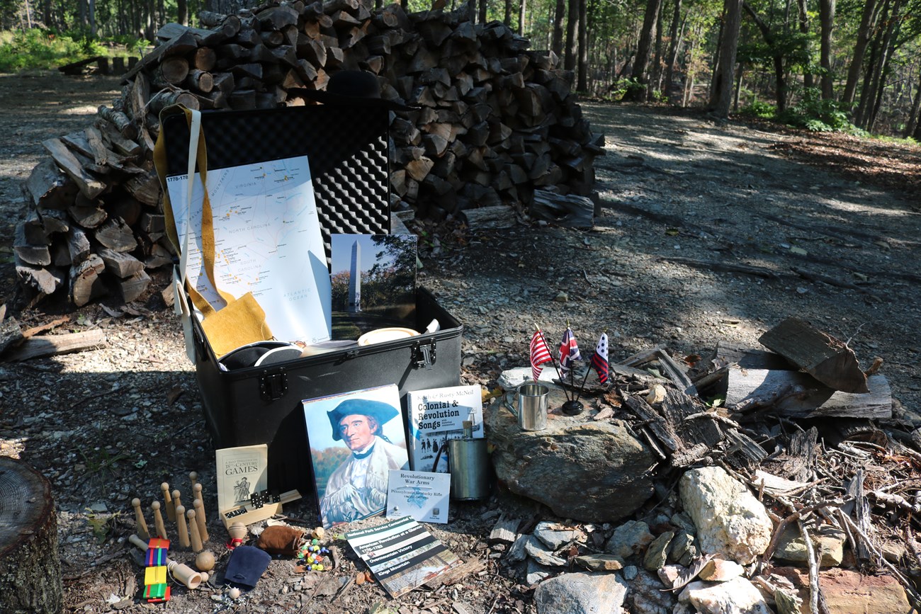 An open trunk with lots of Revolutionary War items are shown with a forest in the background.