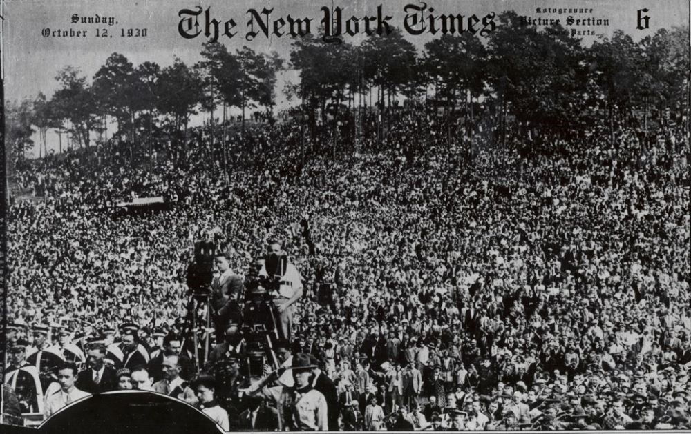 A black and white photograph of thousands of people along a ridge with trees only in the far background.