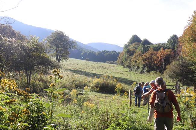 A group hikes along a trail with mountains in the background