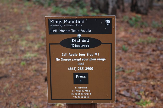 A brown sign for an audio tour with a forest in the background